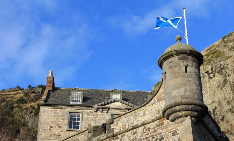 Saltire flying above a stone turret, with a traditional Scottish building below
