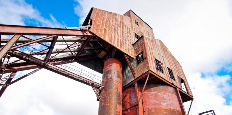 Rusting steel colliery headgear and coal loading structure against a blue sky