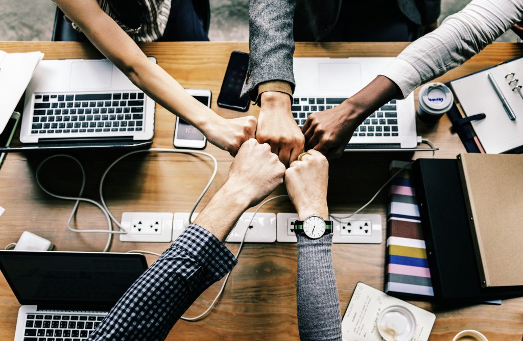 Team members bumping fists over a desk of laptops