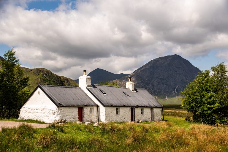 Whitewashed stone cottages at the foot of a steep Scottish hillside