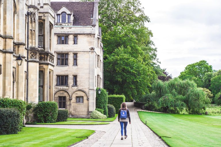 Student walking a path between a historic college building and its lawns